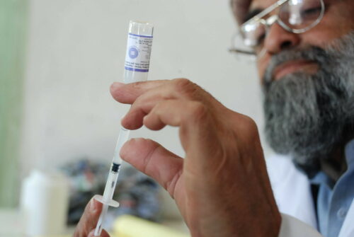 A man draws medication into the syringe he holds in the foreground. 