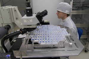 A person wearing a hairnet looks at tiles with a microscope