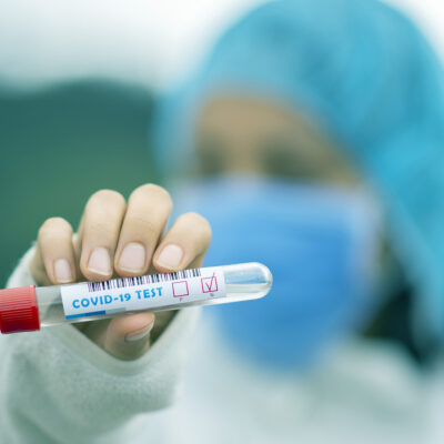 Masked medical worker holding a test tube labeled COVID-19 test